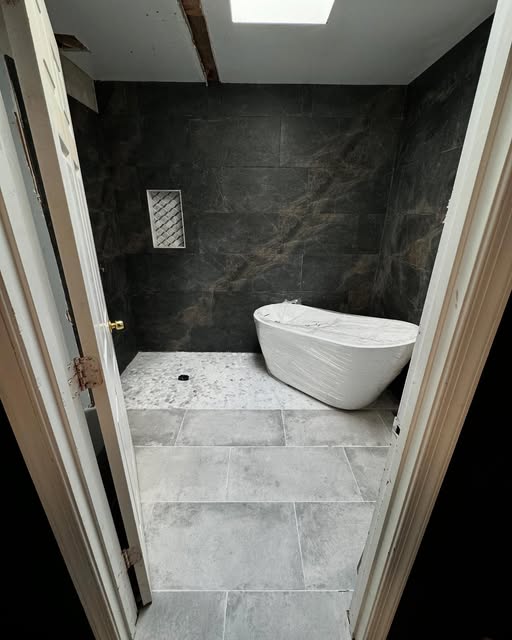 Bathroom with slate wall tiles, a freestanding tub, and skylight