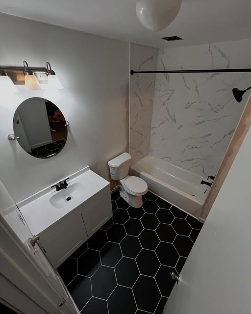 Bathroom with a round mirror and black hexagonal floor tiles